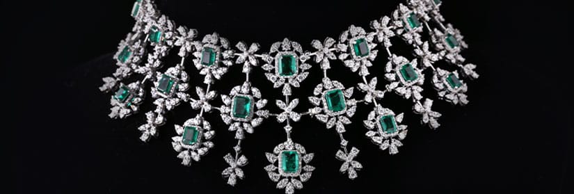 A diamond necklace with emerald gem stone kept before a black background