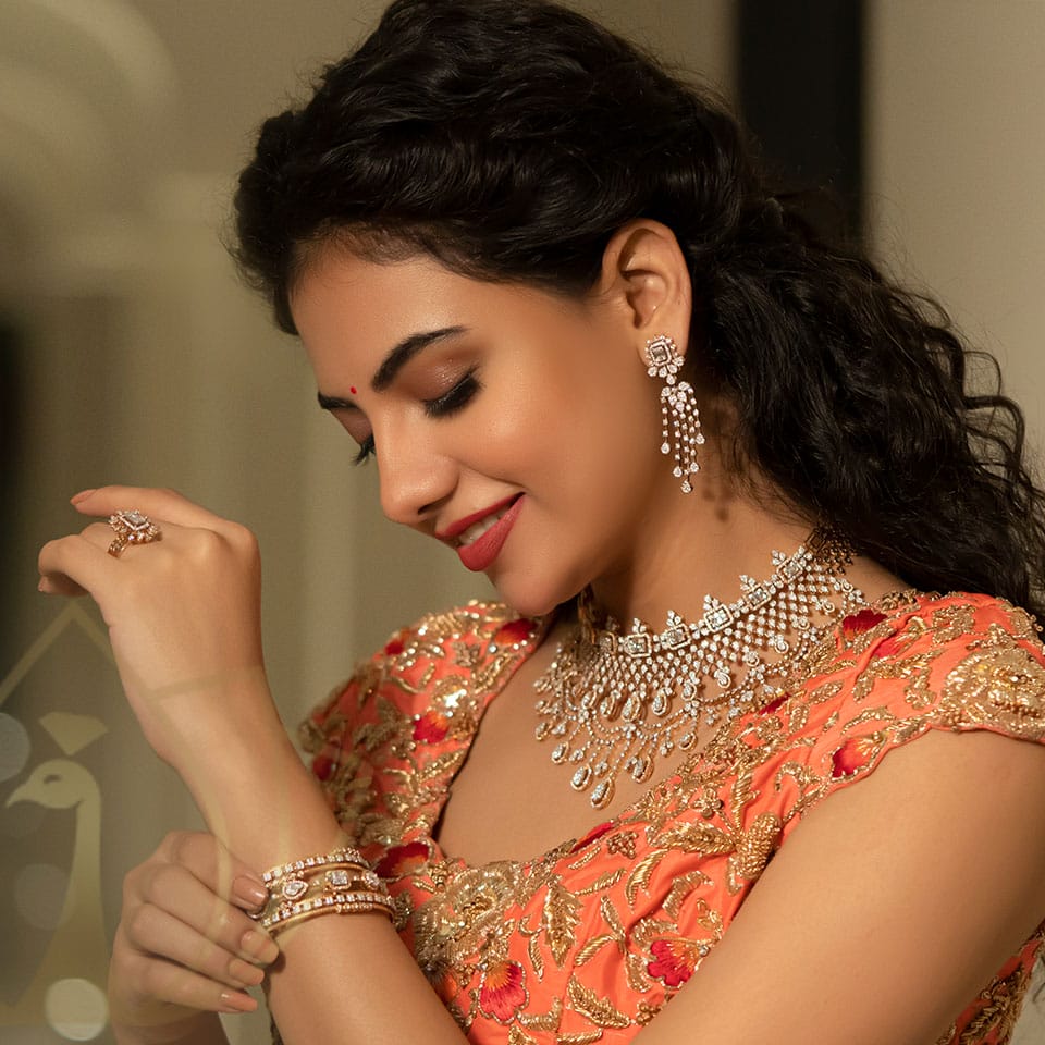 A female model is posing for a photograph with diamond necklace, diamond rings, diamond bangle and diamond earring wearing a orange sleeveless top.