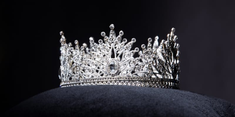 A diamond crown kept on a black cloth in front of a black background.