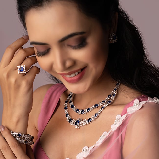 A modern bride wearing a layered necklace, bangles, ring, and earrings studded with diamonds and blue gemstones.